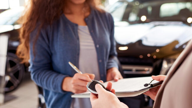 Vício Oculto: Pessoa recebendo a chave de um carro enquanto assina documentos em uma concessionária, representando o momento da compra de um veículo.
